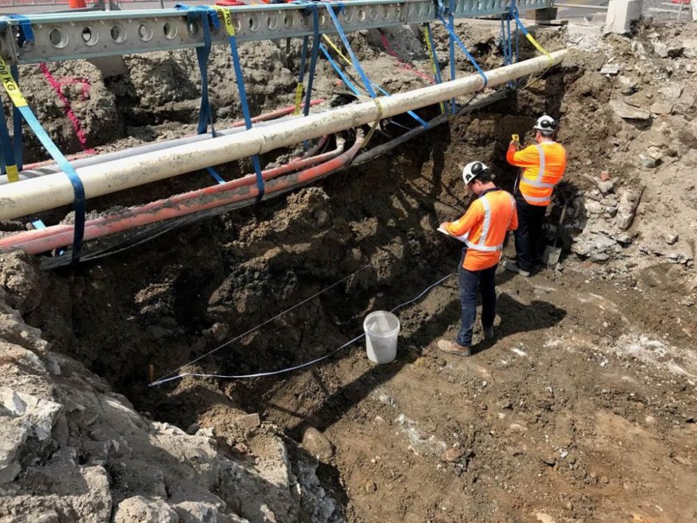 Luke and Angel excavate and record a 19th century sea wall cut into a Māori midden and cultural layer from around the 17th century. The scaffolding above them would later be set up as a lighting rig for their two man show: West Trench Profile.